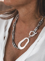 Chunky stainless steel anchor chain necklace with a large irregular abstract pendant, worn against a white top.
