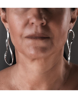 Close-up of a person wearing silver hoop earrings with a neutral background