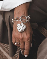 Textured heart charm bracelet in antique-plated silver worn on a model's wrist, showcasing intricate heart detail and toggle clasp.