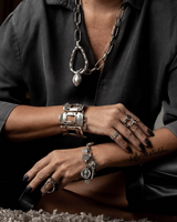 Wide silver-plated zamak arm cuff worn on a model's wrist, featuring five unique linked pieces with an adjustable chain.