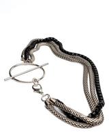 Triple chain necklace featuring steel snake chains and a black aluminum chain, with a large T-clasp at the front.