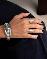 Hand wearing a silver bracelet and multiple rings with black nail polish on a neutral background