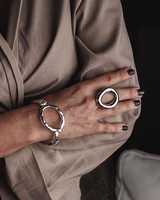 Chunky stainless steel donut ring on a hand with dark nail polish, paired with a bangle bracelet, both presented elegantly.