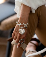Textured heart charm bracelet in antique-plated silver, featuring a detailed heart pendant on a chain, worn on a model's wrist.