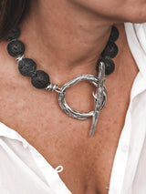 Chunky black lava stone beads with a large silver T-clasp toggle worn as a collar necklace against a casual white shirt.