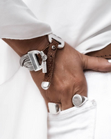 Woven brown leather cuff bracelet with metallic snake chains and engraved charm, worn on a wrist, featuring silver rings.
