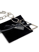 Asymmetrical silver plated statement necklace with a large pendant, chunky carabiner clasp, and textured metallic chain.