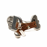 Woven brown leather cuff bracelet with layered silver snake chains and engraved charm, featuring a bold, edgy design.