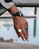 Bold snake chains and woven leather cuff bracelet featuring a neutral leather band and shiny metal accents, worn on a wrist.
