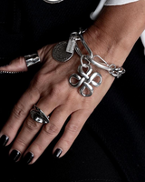 Chunky Cuban link chain bracelet features a bold silver pendant and engraved coin, worn on a model's wrist with rings.