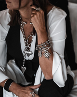 Chunky Cuban link chain bracelet with an engraved coin and sculpted pendant, worn stacked with other silver bracelets.