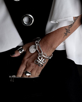 Chunky Cuban link chain bracelet featuring an engraved coin and sculpted pendant, styled on a hand with rings.