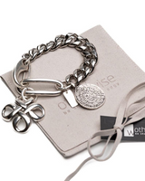 Chunky Cuban link chain bracelet featuring an engraved coin and sculpted pendant, displayed on a suede pouch.
