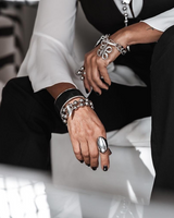 Chunky Cuban link chain bracelet with an engraved coin and sculpted pendant, worn with layered silver and leather jewelry.