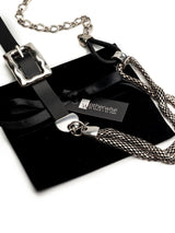 Chunky black leather choker with a large metallic buckle and long steel snake chains, presented on a velvet pouch.