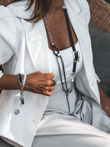 Chunky gothic statement necklace featuring long snake chains and a black leather buckle, worn over a white top and blazer.