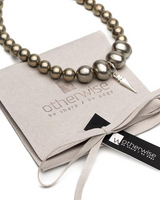 Layered necklace featuring metallic beads in varied sizes and a silver spike pendant, presented on a suede pouch.