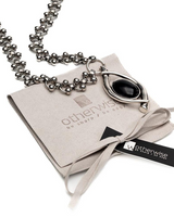 Layered stainless steel necklace featuring round beads and a black oval Murano glass pendant on a suede pouch.