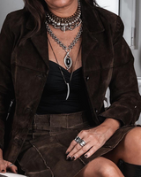 Layered choker and necklaces in gold, silver, and textured finishes worn over a black top, styled with a brown jacket.