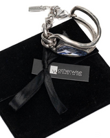 Silver keychain with blue accent on black velvet surface with 'Otherwise' brand tag.