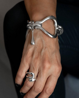 Chunky silver metal cuff bracelet with sculptural links, adjustable fit, worn on the wrist alongside a matching silver ring.