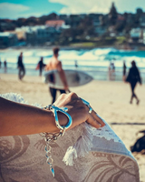 Sculptural silver metal cuff bracelet worn on the wrist, displaying an organic link design against a beach backdrop.
