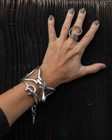 Chunky silver metal cuff bracelet with sculptural link designs worn on a hand against a dark wooden surface.
