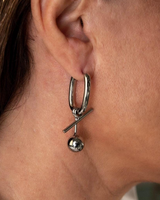 Close-up of a silver hoop earring with a dangling ball on an ear.