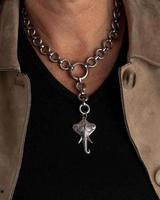 A close-up of a person wearing a chunky silver chain necklace with a dangling elephant charm, styled over a black shirt and tan suede jacket.