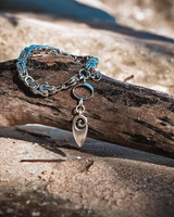 Silver bracelet with a wave charm on a wooden log on a beach