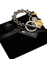 A silver-toned beaded bracelet with a large toggle clasp and gold-toned charms, presented on a black velvet pouch with a black ribbon and a visible Waterwise branding tag.