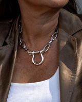 Rhodium-plated silver choker necklace with a textured horseshoe-inspired U bolt, worn with a white top and brown jacket.