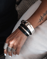 Hand wearing multiple bracelets and rings with a tattoo on the arm.