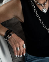 Person wearing a black tank top with a long chain necklace, multiple bracelets, and rings.