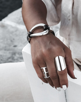 Black leather and irregular silver metal cuff bracelet worn on a model's wrist, featuring chunky design and adjustable fit.