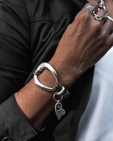 Metal and leather cuff bracelet features irregular silver-plated design with a leather strap, styled on a wrist.