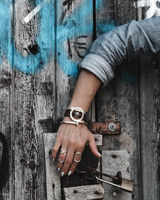 Person's hand with multiple rings on a wooden door with graffiti