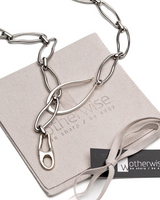 Silver necklace and bracelet set with elongated organic links, featuring a carabiner closure, on a suede pouch.