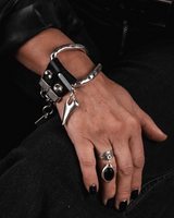 Hand wearing a black leather glove with silver handcuffs and rings on a dark background