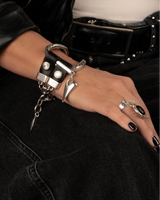 Close-up of a hand wearing a black leather bracelet with metal charms, sitting on black pants.