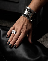 Hand wearing a silver bracelet and ring on a dark fabric background