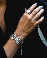 Hand wearing a silver bracelet and ring with turquoise nail polish on a dark background