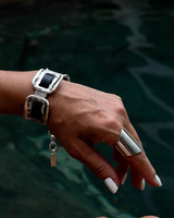 Hand wearing a silver bracelet with a black stone against a blurred natural background