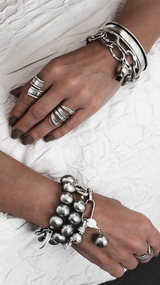 Close-up of hands wearing multiple silver bracelets and rings on a textured white surface