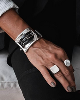 Large metal and leather statement cuff bracelet featuring a chunky sculpted metal link over a black leather band, worn on a wrist.