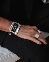 Large metal and leather statement cuff bracelet worn on a wrist, featuring a bold sculpted metal link and dark leather strap.