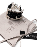 Large metal and leather statement cuff bracelet featuring a sculpted metallic link and dark leather strap, presented on a suede pouch.