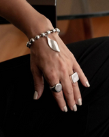 Chunky layered stainless steel bracelets, featuring a ball chain with a leaf pendant and a hammered bangle, worn on a model's wrist.
