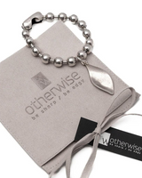 Chunky stainless steel bracelet featuring a ball chain and a Zamak leaf pendant, displayed on a suede pouch.
