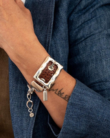 Bold belt buckle bracelet featuring rugged brown leather and shiny silver-plated metal hardware, worn on the wrist.